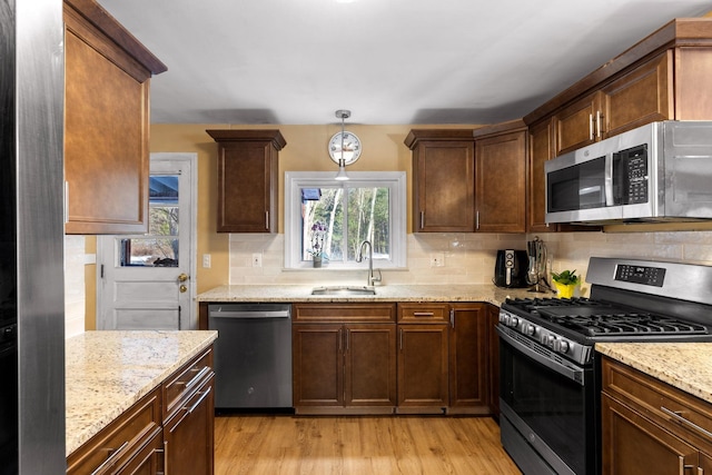 kitchen featuring stainless steel appliances, a sink, light wood-style floors, backsplash, and pendant lighting