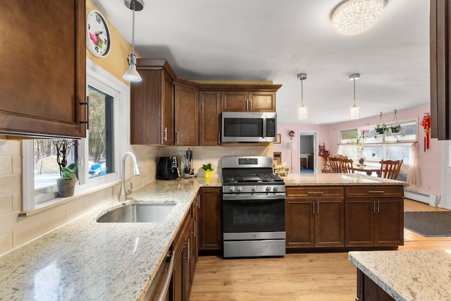 kitchen with light stone countertops, stainless steel appliances, a sink, and decorative light fixtures