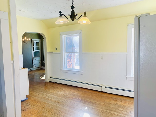 dining area with arched walkways, wainscoting, wood finished floors, baseboard heating, and a chandelier