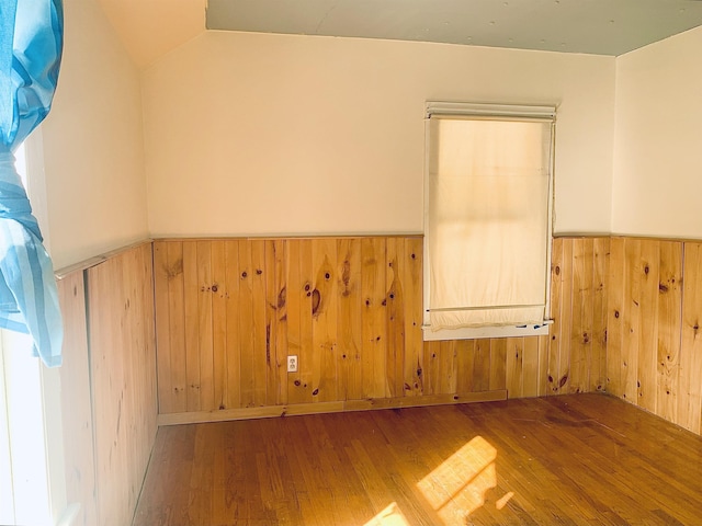 empty room featuring lofted ceiling, wainscoting, wooden walls, and wood finished floors