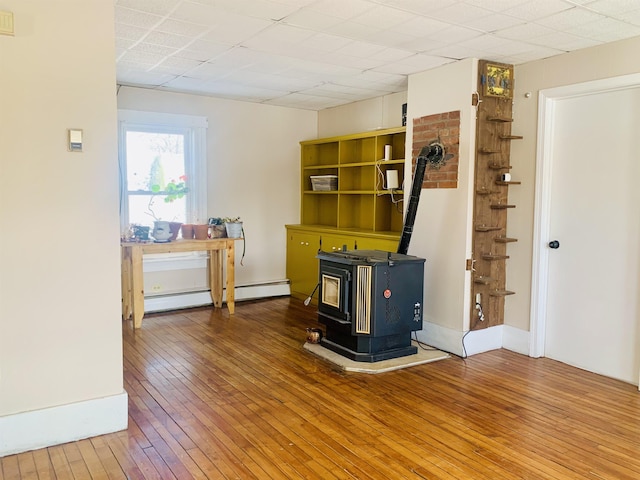 interior space with baseboards, a drop ceiling, a baseboard radiator, wood finished floors, and a wood stove