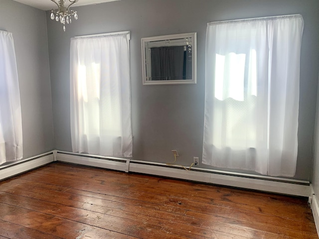 spare room with dark wood-style floors, a baseboard heating unit, and an inviting chandelier