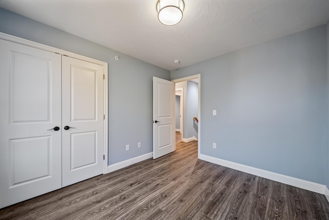 unfurnished bedroom with a closet, baseboards, and dark wood-style flooring