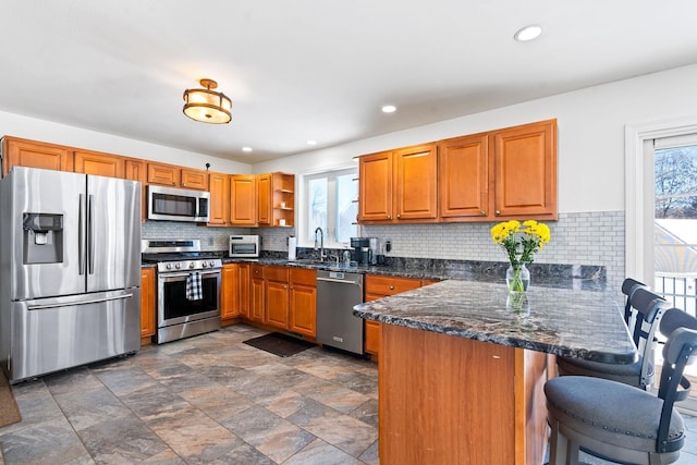 kitchen with a breakfast bar area, open shelves, appliances with stainless steel finishes, brown cabinetry, and a peninsula