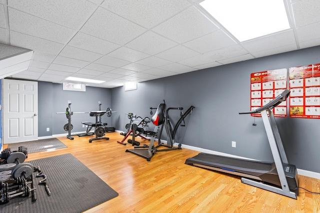 workout area featuring wood finished floors, a paneled ceiling, and baseboards