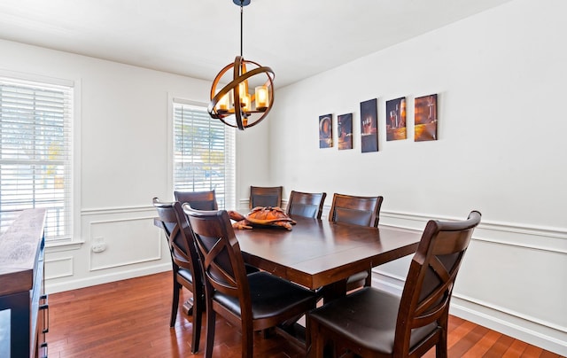 dining area with an inviting chandelier, a decorative wall, dark wood-type flooring, and wainscoting