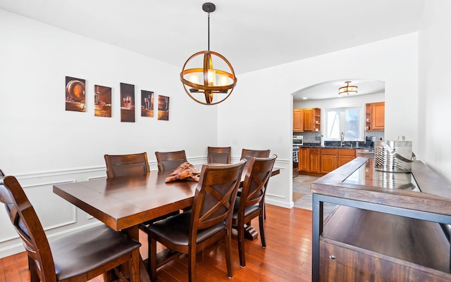 dining area featuring arched walkways, a notable chandelier, and light wood-style flooring