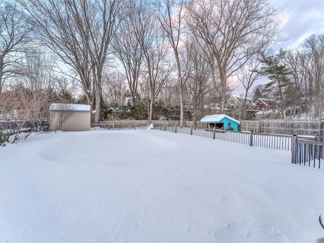 yard layered in snow with a storage shed, fence, and an outdoor structure