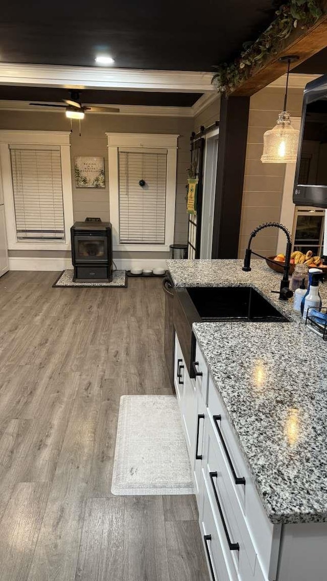 kitchen with dark wood-style flooring, white cabinetry, light stone countertops, a wood stove, and pendant lighting