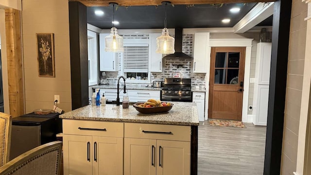 kitchen featuring light stone counters, white cabinets, appliances with stainless steel finishes, wall chimney exhaust hood, and decorative light fixtures