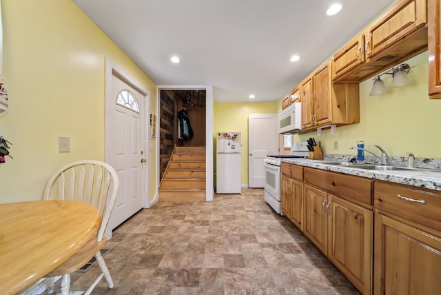 kitchen with white appliances, brown cabinetry, light stone counters, a sink, and recessed lighting