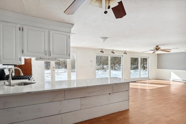 kitchen featuring a ceiling fan, white cabinetry, a sink, a textured ceiling, and light wood-type flooring