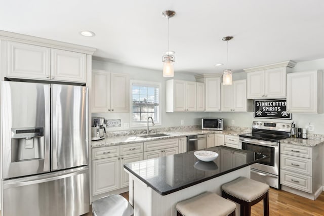 kitchen featuring stainless steel appliances, a sink, a center island, hanging light fixtures, and light stone countertops