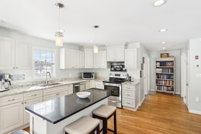 kitchen featuring decorative light fixtures, a center island, stainless steel appliances, white cabinetry, and a sink