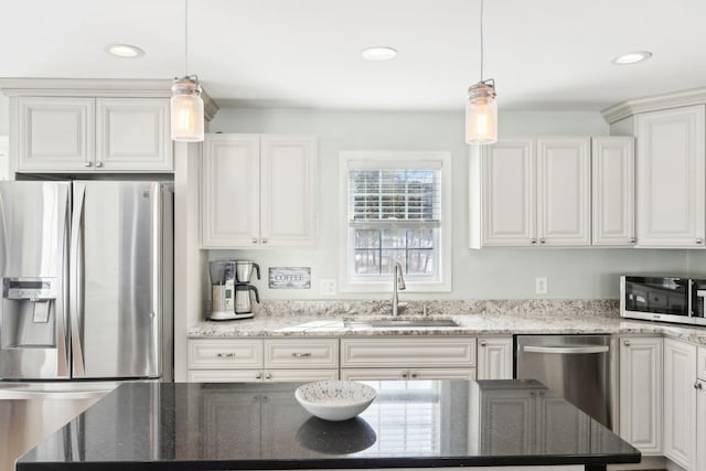 kitchen with appliances with stainless steel finishes, white cabinets, a sink, and hanging light fixtures