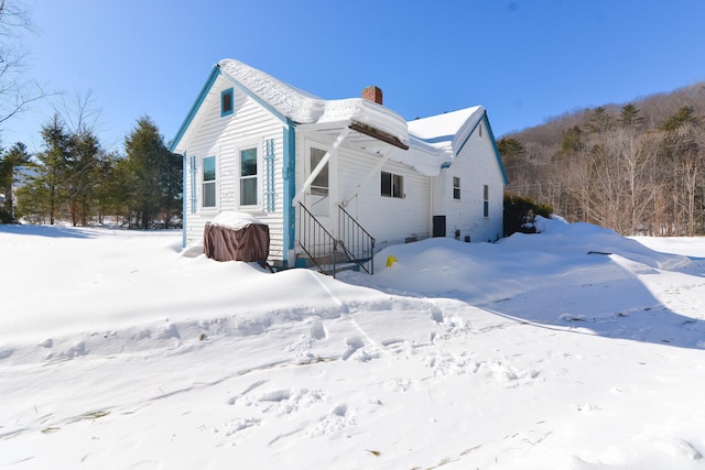 snow covered rear of property featuring a garage and a chimney