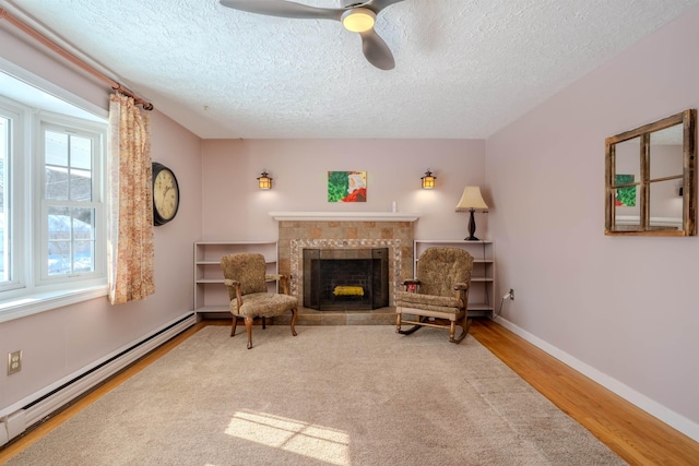 living area with baseboards, a tile fireplace, a baseboard radiator, ceiling fan, and wood finished floors