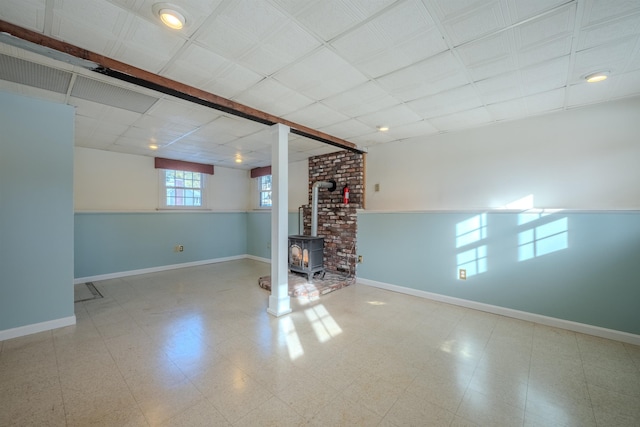 basement featuring tile patterned floors, a wood stove, and baseboards