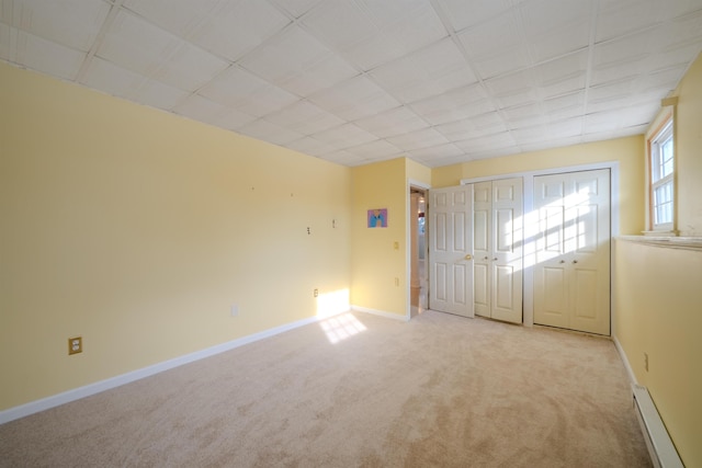 unfurnished bedroom featuring light carpet, baseboards, baseboard heating, and multiple closets