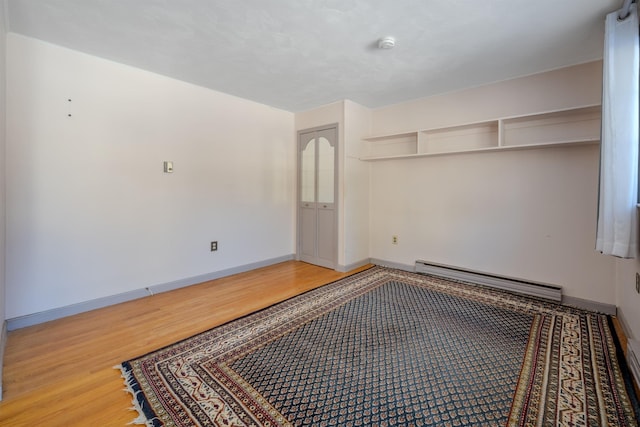 unfurnished bedroom with a baseboard heating unit, wood finished floors, and baseboards