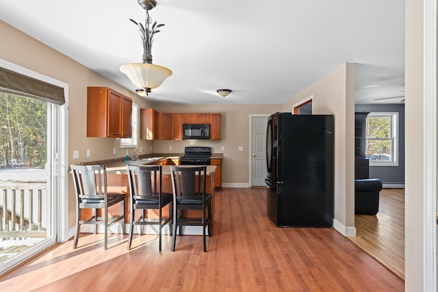 kitchen with hanging light fixtures, brown cabinetry, black appliances, light wood-type flooring, and baseboards