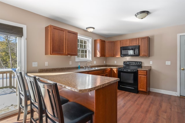 kitchen with black appliances, brown cabinetry, a peninsula, and a sink