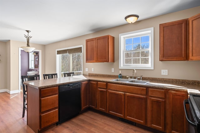 kitchen featuring a peninsula, a sink, hanging light fixtures, brown cabinets, and black appliances