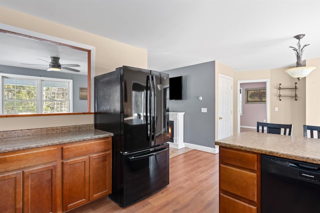 kitchen featuring a warm lit fireplace, light wood finished floors, brown cabinetry, decorative light fixtures, and black appliances