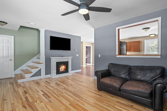 living area with baseboards, a glass covered fireplace, a ceiling fan, and light wood-style floors