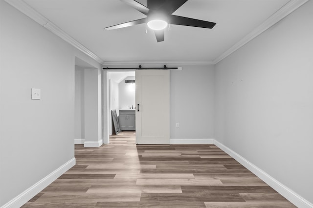 unfurnished room with baseboards, a barn door, a ceiling fan, and crown molding