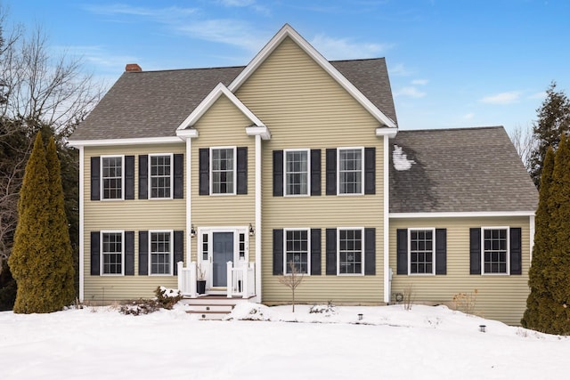 colonial-style house featuring roof with shingles and a chimney