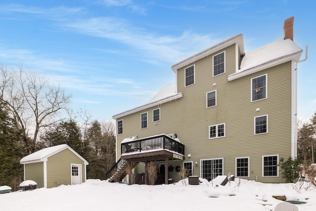 snow covered back of property featuring a chimney, stairway, a deck, and an outdoor structure