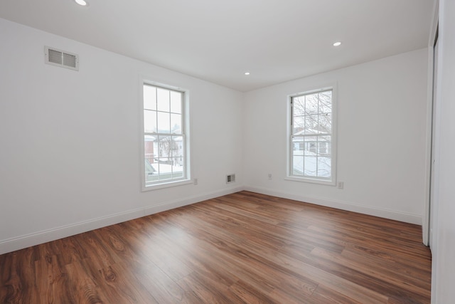 empty room with dark wood-type flooring, visible vents, and baseboards