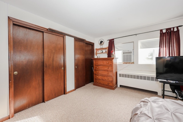 bedroom with multiple closets, light carpet, and radiator heating unit