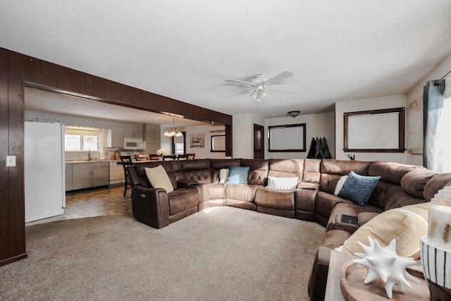 living room featuring ceiling fan with notable chandelier, wood walls, and light colored carpet