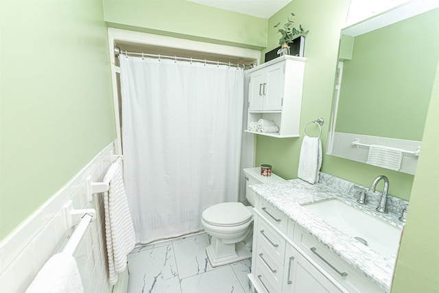 full bathroom featuring toilet, marble finish floor, a wainscoted wall, and vanity