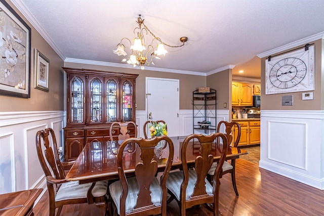 dining room featuring a chandelier, a wainscoted wall, a textured ceiling, and wood finished floors