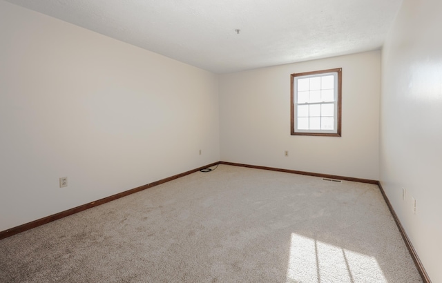 empty room featuring light carpet, visible vents, and baseboards