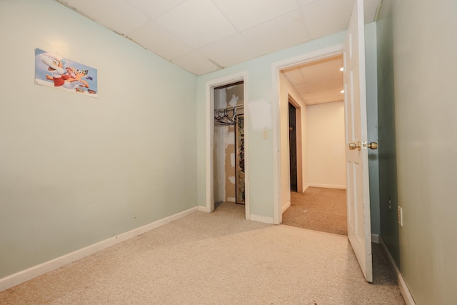 unfurnished bedroom with a paneled ceiling, baseboards, a closet, and light colored carpet