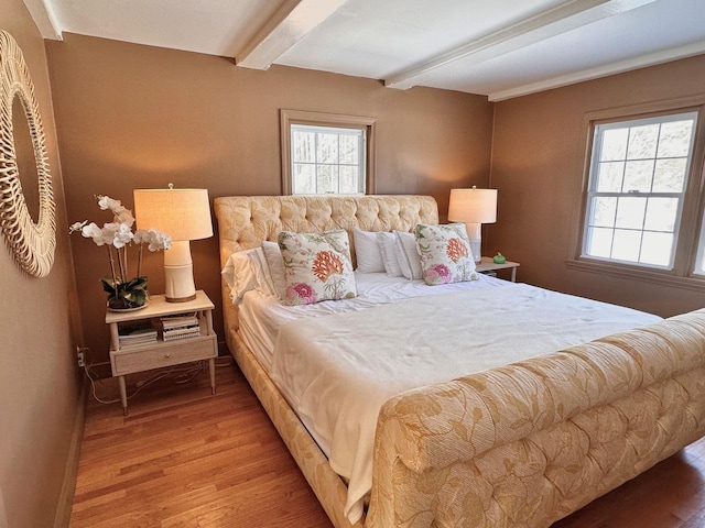 bedroom with beam ceiling, baseboards, and wood finished floors