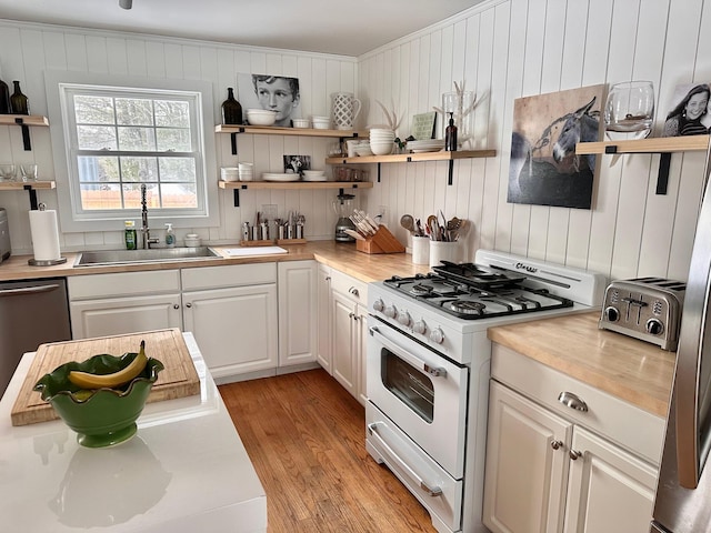 kitchen with light wood finished floors, white range with gas stovetop, white cabinetry, open shelves, and a sink