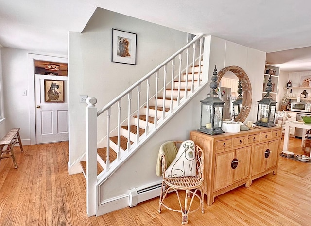 stairway featuring a baseboard radiator, baseboards, and wood finished floors