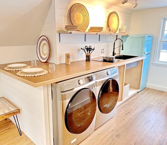 clothes washing area with laundry area, baseboards, light wood-style flooring, washing machine and clothes dryer, and a sink