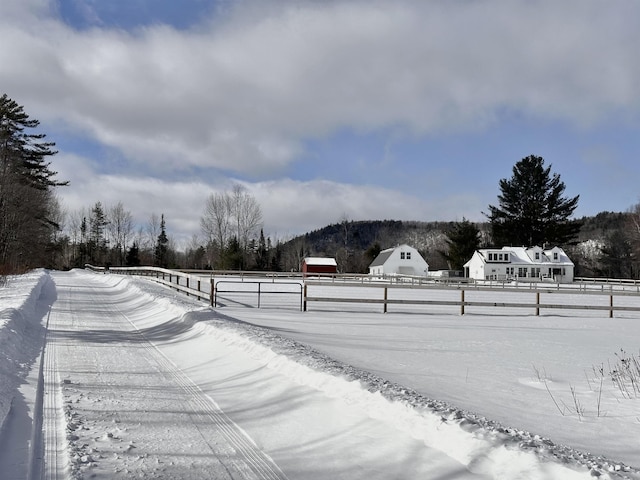 snowy yard with a rural view and fence