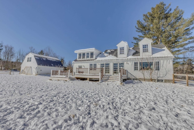 snow covered house with a deck, an outbuilding, and a barn