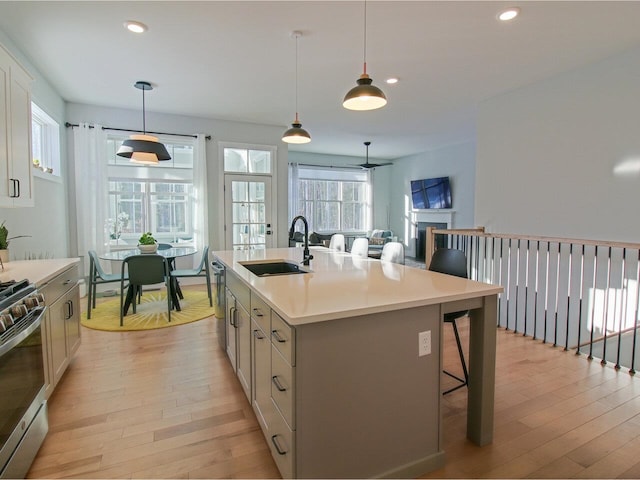 kitchen featuring stainless steel range with gas cooktop, light countertops, hanging light fixtures, a sink, and an island with sink