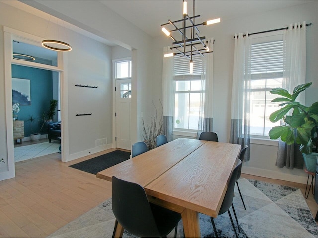 dining area with a healthy amount of sunlight, light wood-style flooring, baseboards, and a notable chandelier