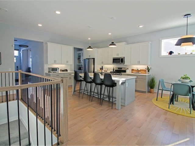 kitchen featuring appliances with stainless steel finishes, decorative light fixtures, a kitchen island with sink, light countertops, and white cabinetry