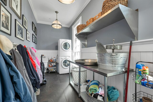 washroom featuring stacked washer / drying machine, laundry area, a wainscoted wall, and crown molding