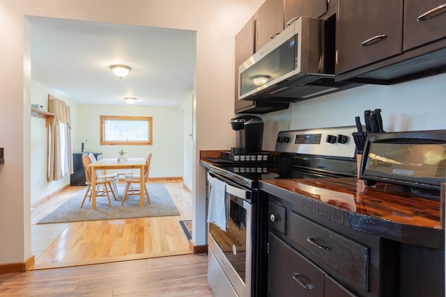 kitchen featuring dark brown cabinetry, baseboards, dark countertops, stainless steel appliances, and light wood-type flooring